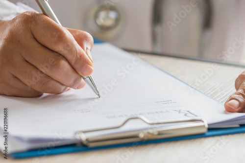 Healthcare medical concept, Hands Doctor's writing and working on prescription clipboard with record information paper folders on desk in hospital or clinic. Selective focus