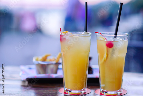 Still life  two glasses of a cold fresh lemonds with ice cubes and drinking straws on a table  bucket with french fried potato in background. Drinks for a friends meeting or date