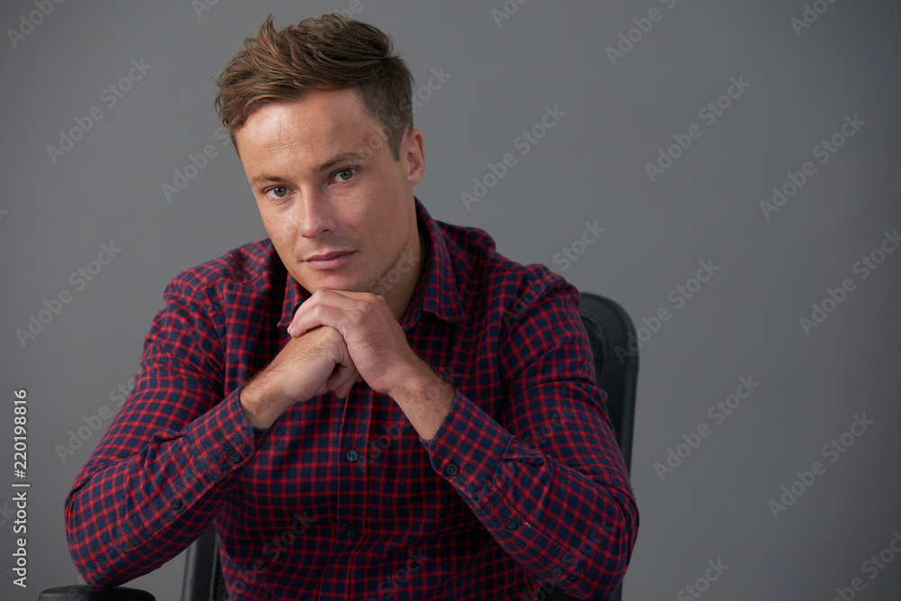 Pensive handsome young man sitting and chair and looking at camera Pensive handsome young man sitting and chair and looking at camera