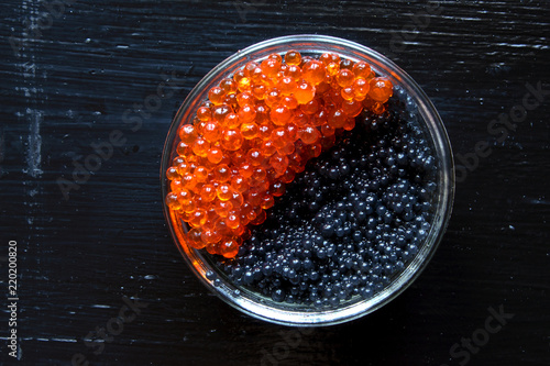 Bowl with black and red caviar on a black wooden table, top view
