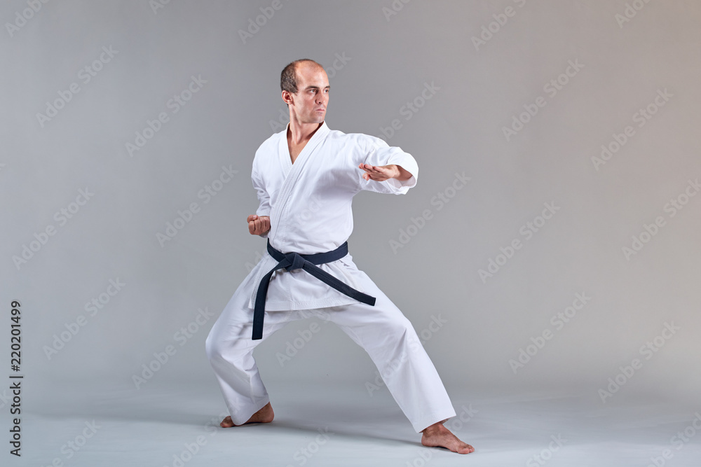 A man in karategi trains a formal karate exercise on a gray background A man in karategi trains a formal karate exercise on a gray background