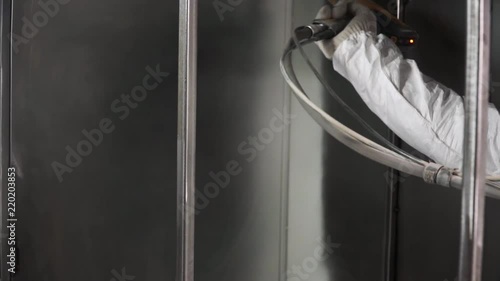 Worker at factory painting metal details with a gun of powder coating. Clip. Construction worker spray paints while wearing respiratory safety equipment to protect himself from the fumes at a factory photo