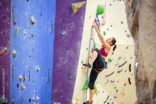 Photo of sportswoman in training on purple wall for rock climbing
