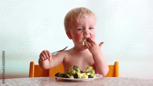 baby eats with pleasure steamed broccoli by fork and hand, happy kid, white background  