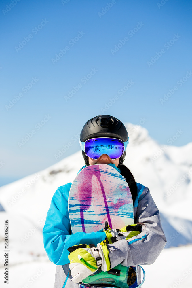 Φωτογραφία Photo of young tourist girl in helmet looking into camera with snowboard in hand