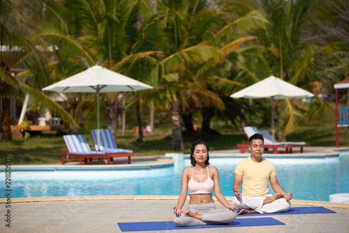 Young Asian couple meditating by swiming pool © DragonImages