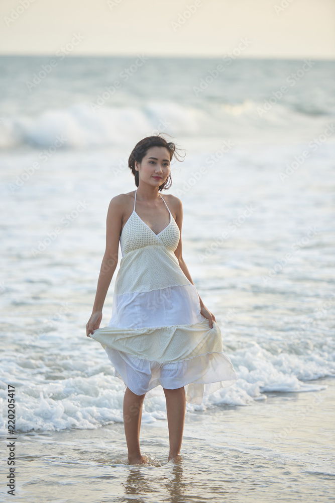 Beautiful young Asian woman in white summer dress walking on beach