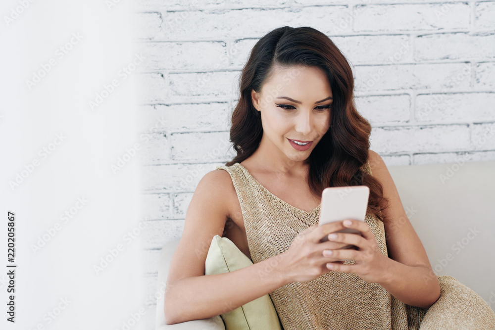 Beautiful attractive young woman sitting on sofa and texting her friends Beautiful attractive young woman sitting on sofa and texting her friends
