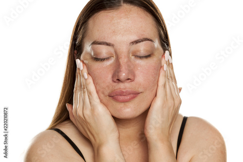 beautiful middle-aged woman applying moisturizer on her face on white background photo