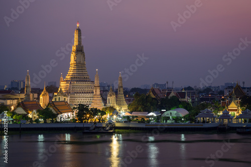 Beautiful view of lit Wat Arun temple next to Chao Phraya River in Bangkok  Thailand  at dusk.