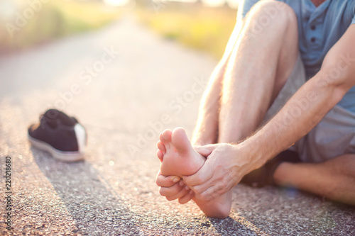 Healthcare, medicine and people concept. Man sitting on the ground suffering from pain in feet