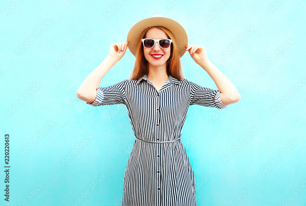 Fashion smiling woman wearing a striped dress, summer straw hat on blue background Fashion smiling woman wearing a striped dress, summer straw hat on blue background