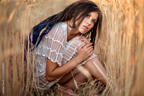 photo shoot of a girl with dreadlocks in a white dress in wheat. the girl is sitting in the wheat