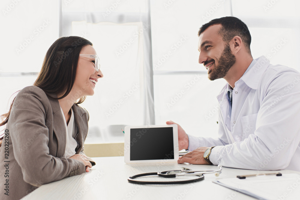 smiling doctor showing patient tablet with blank screen in clinic smiling doctor showing patient tablet with blank screen in clinic