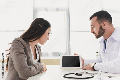 doctor showing patient gadget with blank screen in clinic