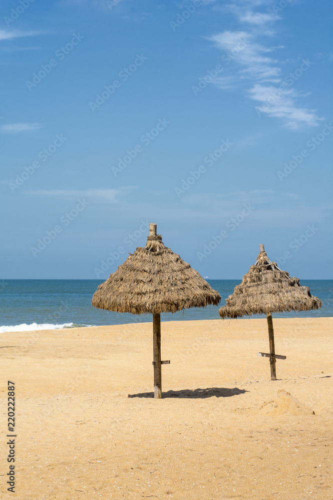 Two parasols on the beach, made of straw, near the water in the sunny day Two parasols on the beach, made of straw, near the water in the sunny day