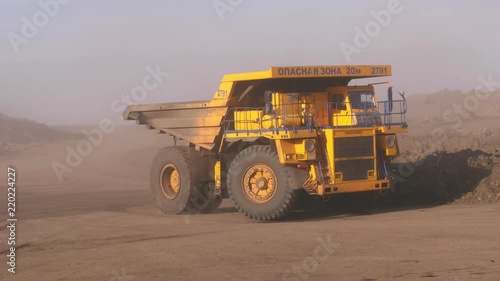Gigantic trucks go around the bend. Huge mining truck rides on a quarry. The truck rides on off-road raising clouds of dust. Close up.