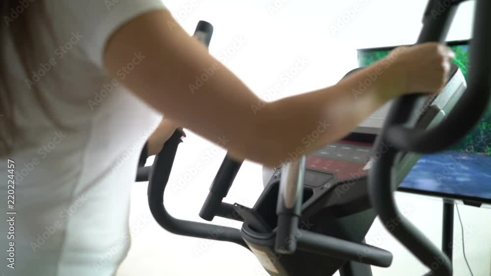 Woman during cardio workout on an elliptical trainer in front of the TV Woman during cardio workout on an elliptical trainer in front of the TV