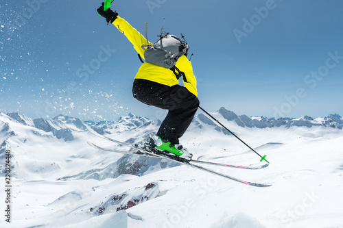 A skier in full sports equipment jumps into the abyss from the top of the glacier against the background of the blue sky and the Caucasian snow-capped mountains. View from the back. Elbrus region