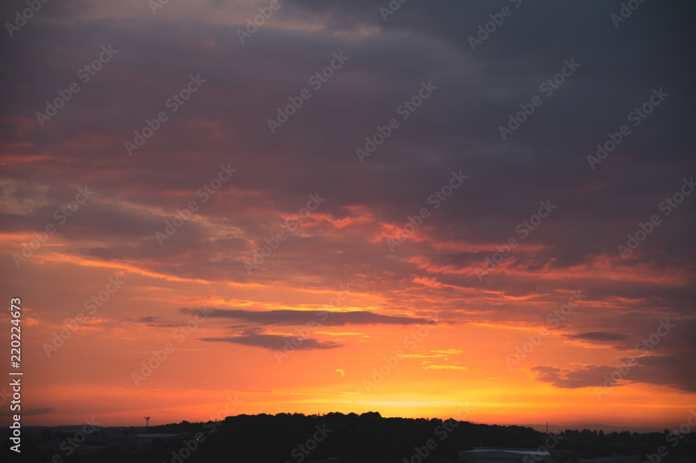 Evening sky after sunset with red clouds and the silhouette of the private sector of a small town