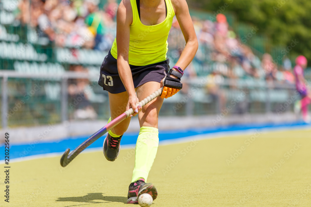 Fototapeta premium Young girl playing field hockey running with stick and ball