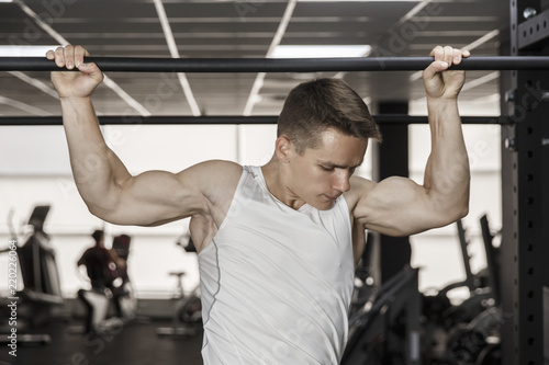 Guy bodybuilder execute exercise pulling up on horizontal bar in gym, horizontal photo