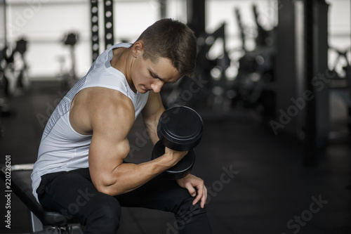 Muscular man working out in gym doing exercises with dumbbells at biceps, strong male torso