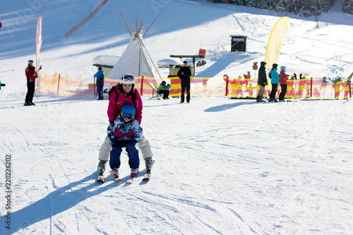 Young mother, teaching her preschool child to ski, sunny winter day