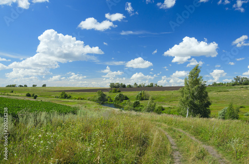 Sunny summer landscape with country road,fields,green hills and beautiful clouds in blue sky.River Upa in Tula region,Russia.