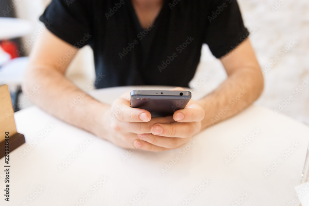 Handsome, young man using his mobile phone in a public area, at the table