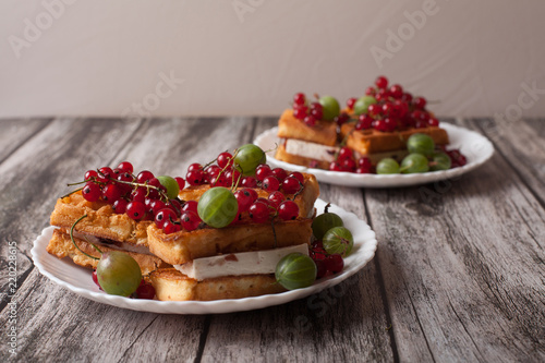 Viennese waffles with berries of red currants and gooseberries lie on a plate on a wooden table