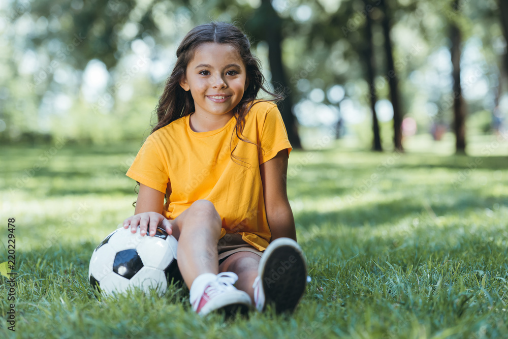 cute happy child sitting on grass with soccer ball and smiling at camera cute happy child sitting on grass with soccer ball and smiling at camera