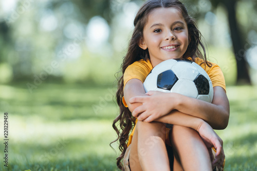 adorable happy child holding soccer ball and smiling at camera in park photo