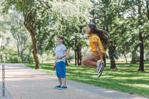 Photography adorable happy kids playing and jumping with skipping ropes in park