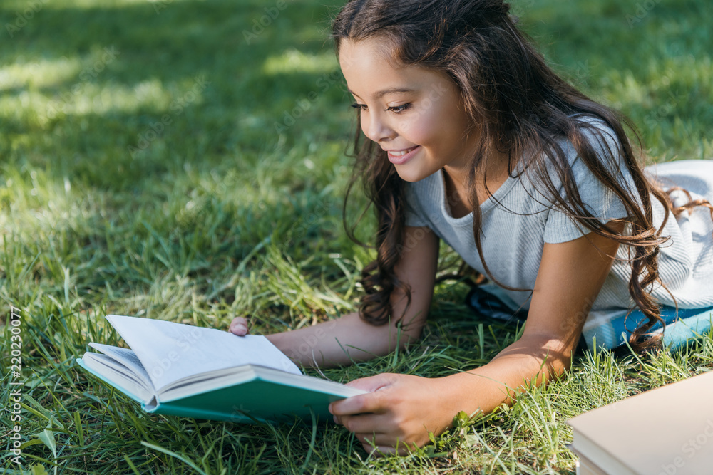 cute smiling child lying on grass and reading book cute smiling child lying on grass and reading book