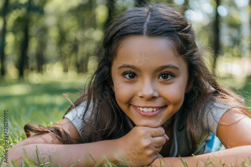 adorable happy child lying on grass and smiling at camera in park