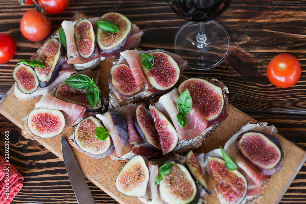 Healthy bruschettas with bread, cream cheese, prosciutto, figs and basil on rustic wooden table