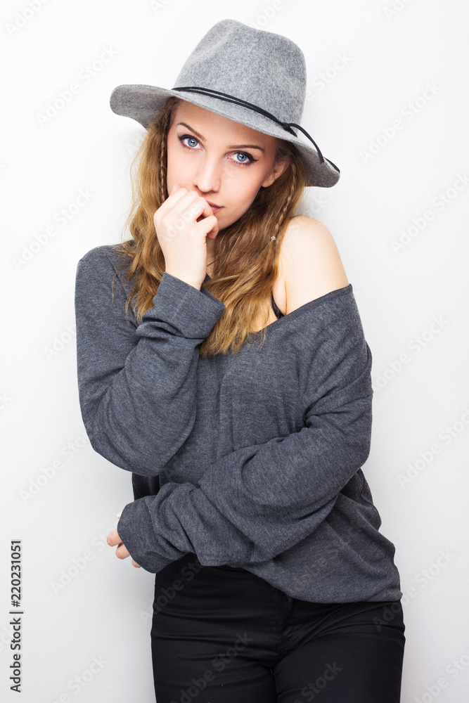 Young woman in oversize gray blouse and wide brim hat, posing against white background