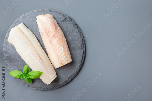 Fotografia Fresh raw cod fillet with basil on stone plate, horizontal, copy space, top view