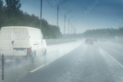White van rides on the road. Strong rain and water drops