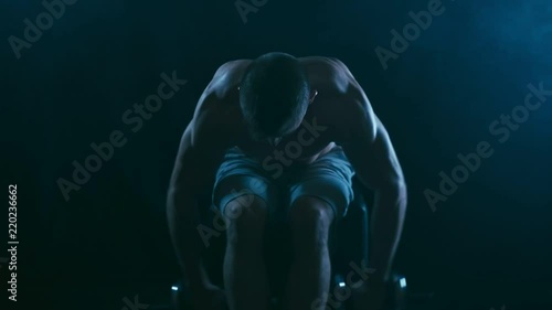 Fitness man on black, doing Reverse Flyes for back delts, with blue smoke on background