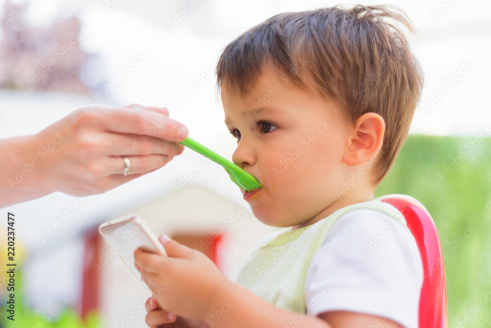 Baby eating the lunch while looking at the smartphone Baby eating the lunch while looking at the smartphone
