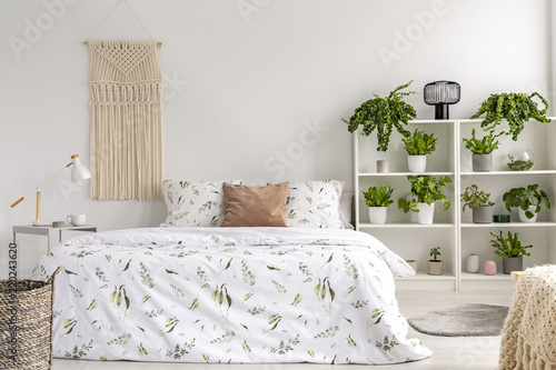 Close to nature bright bedroom interior with many green plants beside a big bed. Woven tapestry above the bed. Real photo.