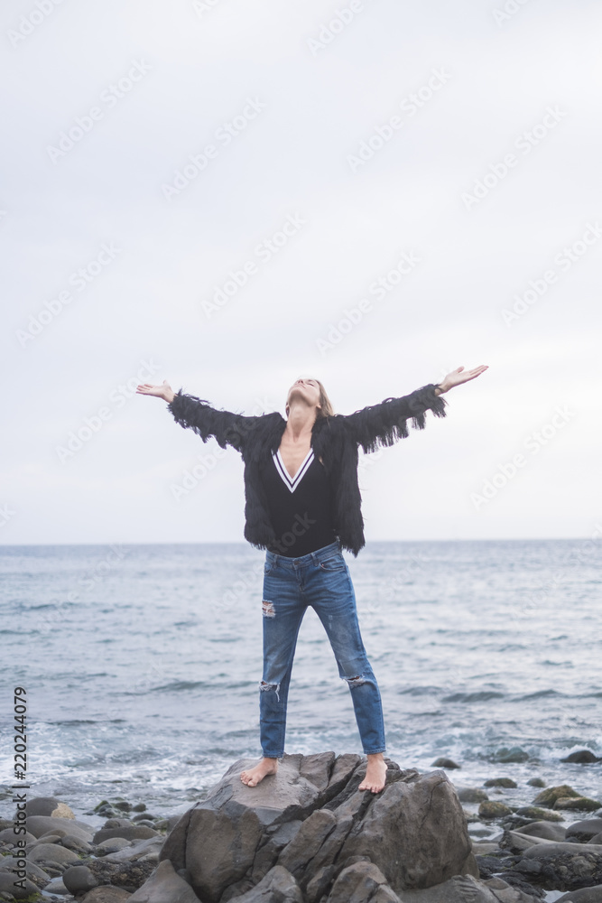 beautiful young woman standing on a rock at the beach looking the sky and enjoying the power of the nature and the feeling of the travel. freedom and lifestyle for nice girl beautiful young woman standing on a rock at the beach looking the sky and enjoying the power of the nature and the feeling of the travel. freedom and lifestyle for nice girl
