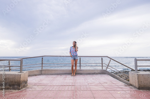 beautiful young lady caucasian woman standing at the beach on the road listening music with headphone and enjoying the leisure activity. vacation and lifestyle concept for nice people