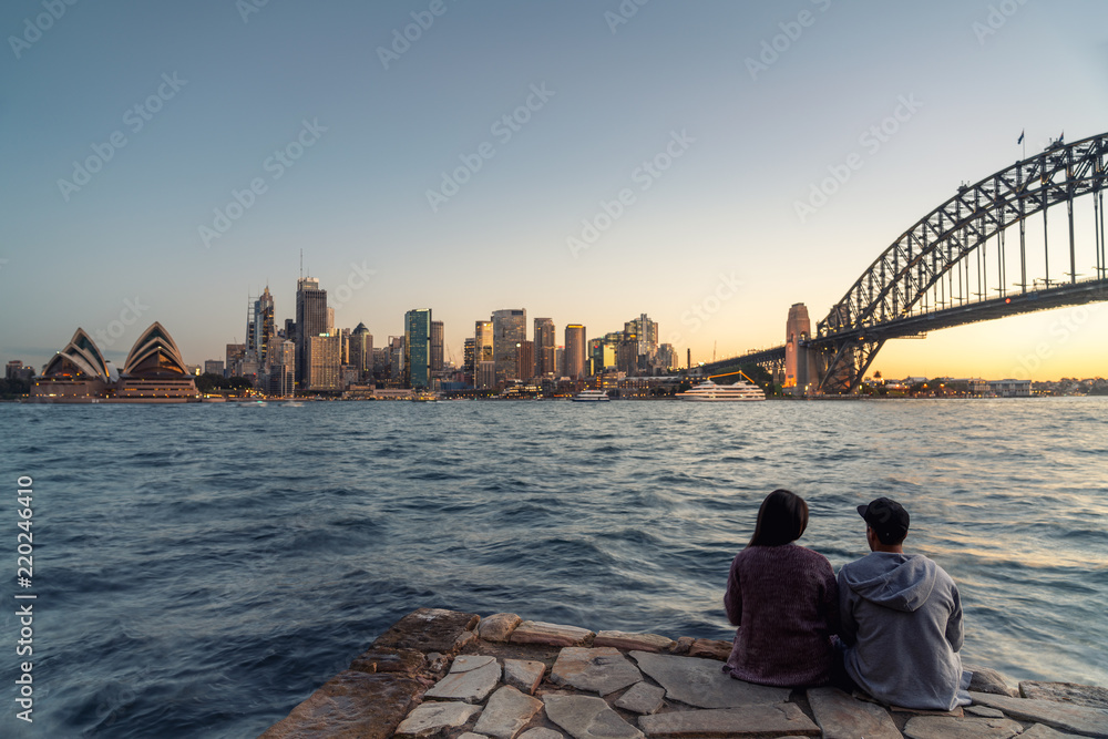 Naklejka premium Romantyczna para patrzy na panoramę Sydney o zmierzchu w Sydney, Nowa Południowa Walia, Australia.