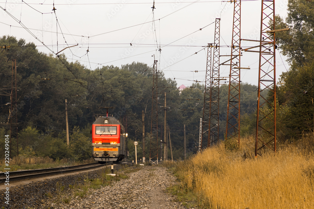 A red electric train without rolling stock leaves along the railroad tracks into the distance