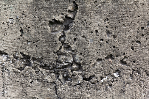 Porous with small cracks gray concrete wall, with protruding pebbles from the inside