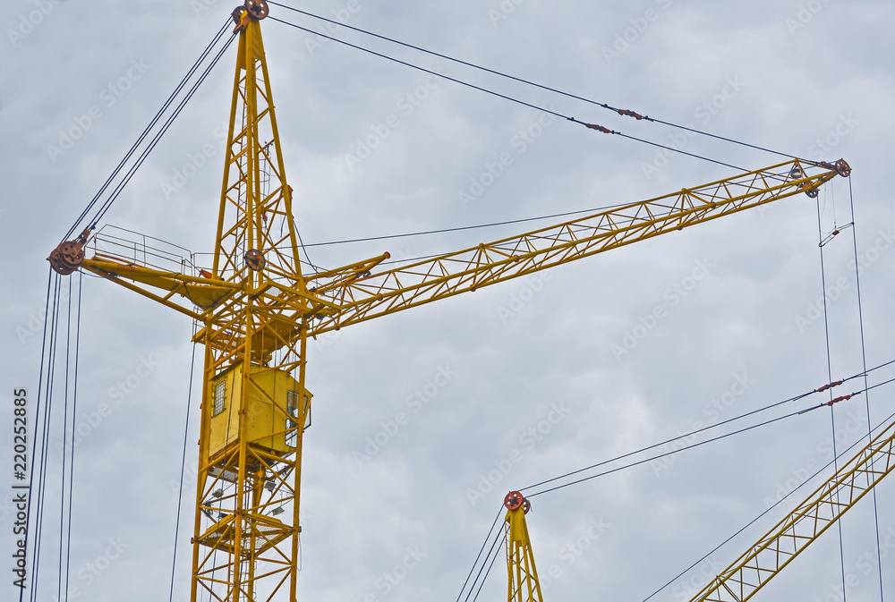 Two yellow construction crans on the cloudy sky background, the view from the bottom up Two yellow construction crans on the cloudy sky background, the view from the bottom up