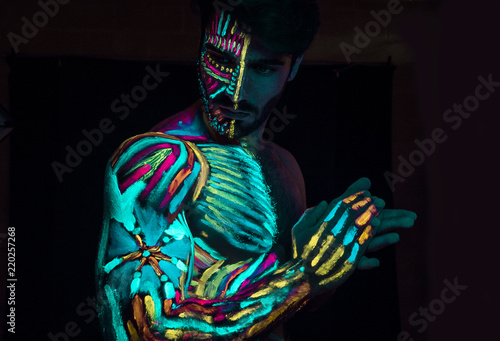 фотографія Young man painted in fluorescent paint on face and muscular torso, in studio sho
